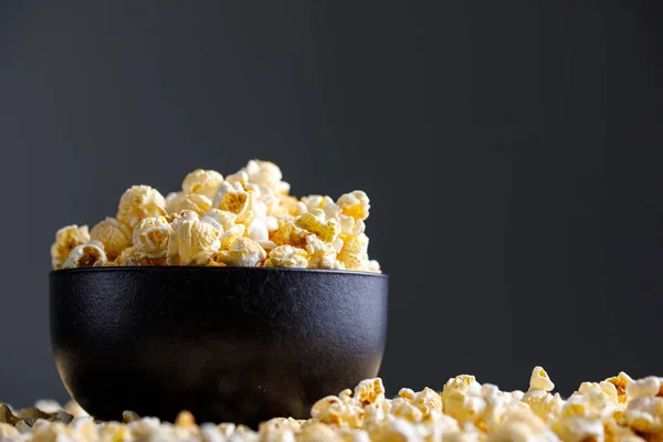 Popcorn v Černé keramické mísy a kolem něj. — Stock fotografie