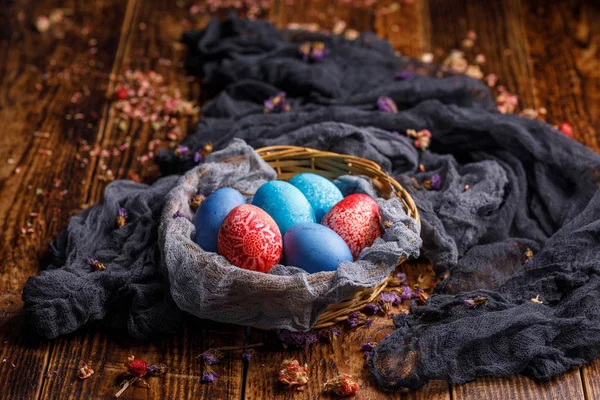 Cesta de mimbre con huevos de colores en diferentes colores sobre un fondo de madera . — Foto de Stock