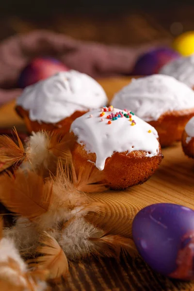 Påsk Stilleben med cupcakes i vit glasyr och ovanligt målade ägg, dekorerad med fjädrar på en trä bakgrund. — Stockfoto