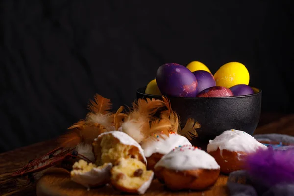 Bakning i vit glasyr och ovanligt målade ägg i en keramisk kopp med grejor dekorationsfjädrar. — Stockfoto
