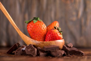 Ahşap arka plan üzerinde kırık çikolata dilim çevrili bir tahta kaşık büyük taze çilek. Makro.