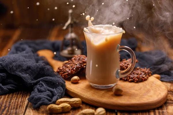 Té con galletas en una taza de vidrio con un chapoteo. Fumar, té con leche y galletas de chocolate con nueces para el desayuno se derraman de la taza . —  Fotos de Stock