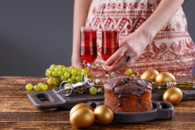 Kız Festival tablo Easter için yatıyor. Taze ev Paskalya kek, altın yumurta, kırmızı şarap vintage gözlük, üzüm ve antika tirbuşon masada.