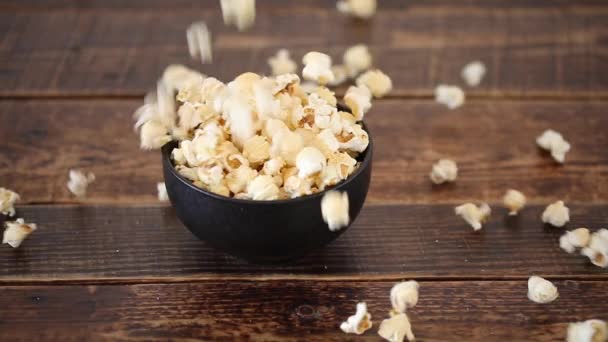 Popcorn tombe dans un bol noir sur un fond en bois. Blanc morceaux moelleux de pop-corn tombent à un rythme lent, verser dans la tasse par en bas et rebondir l'un l'autre .