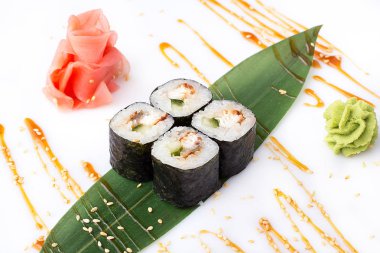 Lezzetli taze mini-salatalık, yılan balığı ve peynir ile bir muz yaprağına rulo. Zencefil ve wasabi ile beyaz bir arka plan üzerinde suşi rulo.