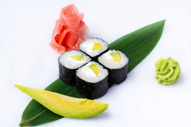 Lezzetli taze mini-avokado ve peynir üzerinde rulo bir muz yaprağı. Zencefil ve wasabi ile beyaz bir arka plan üzerinde suşi rulo.