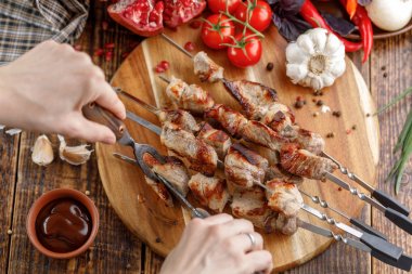 Rustik natürmort. Sulu domuz eti bir bıçak ve çatal ile kesilir. Ahşap arka plan üzerinde taze sebze ve iştah açıcı şiş kebap.