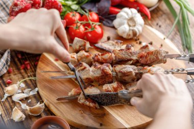 Rustik. Eller bir sulu domuz eti bir bıçak ile kesmek. Ahşap arka plan üzerinde taze sebze ve iştah açıcı şiş kebap. Natürmort.