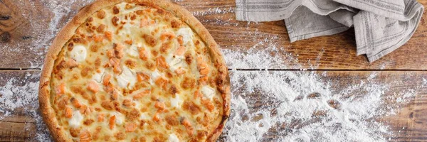 Pizza mit Lachs und Käse auf einem Holzboden mit Mehl. Nahaufnahme. das Konzept des leckeren Essens. Blick von oben. — Stockfoto