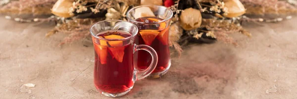 Two glasses of christmas mulled wine with oranges and spices on a textural background. Selective focus. Copy space. Banner. — Stock Photo, Image