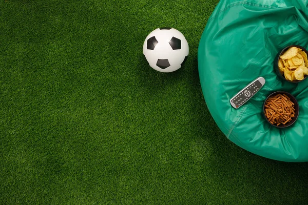 Soccer ball on a green field and ottoman for a fan with snacks a
