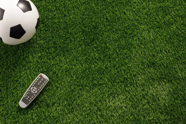 Bola de futebol em um campo verde e um controle remoto de TV. Depósito plano c — Fotografia de Stock