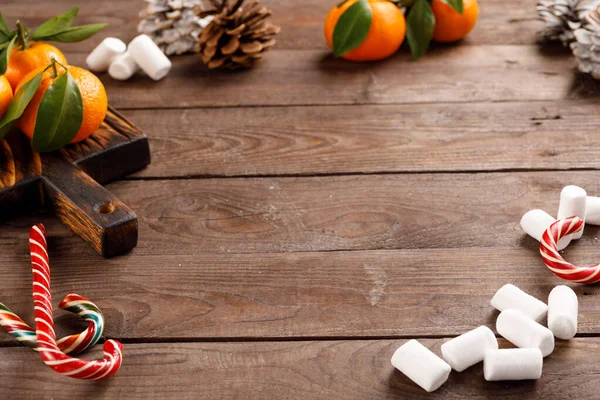 Rahmen aus weihnachtlichem Marshmallows-Weihnachtsschmuck und Mandarinen auf einem hölzernen Hintergrund. Winterurlaub, Neujahrsstimmung. Kopierraum. — Stockfoto