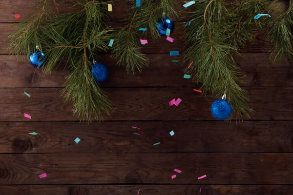 Weihnachtsbaumzweige auf einem hölzernen Hintergrund. Eine Dekoration aus Weihnachtskugeln in einem trendigen klassischen Blau und buntem Konfetti strömt. Kopierraum. — Stockfoto