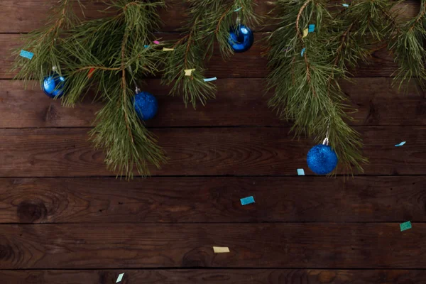 Weihnachtsbaumzweige auf einem hölzernen Hintergrund. Eine Dekoration aus Weihnachtskugeln in einem trendigen klassischen Blau und buntem Konfetti strömt. Kopierraum. — Stockfoto