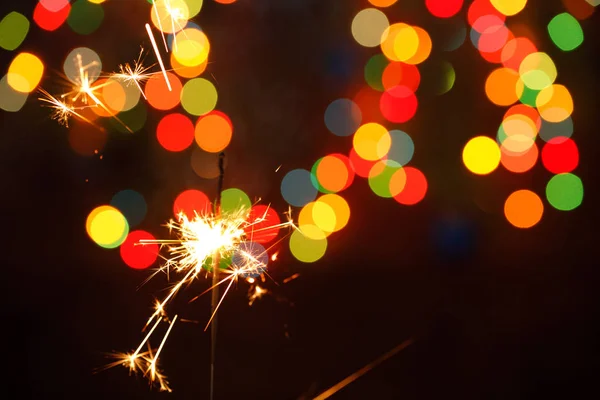 Beautiful sparklers on the background of a garland. beautiful holiday card for the New Year. — Stock Photo, Image