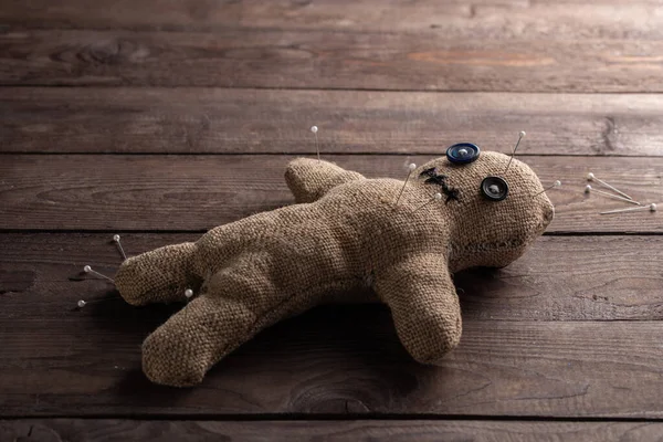 Voodoo doll on a wooden background with dramatic lighting. The concept of witchcraft and black art. Burlap doll on a wooden background. Pierce with maces. Copy space.