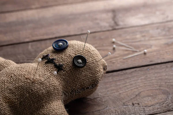 Voodoo doll on a wooden background with dramatic lighting. The concept of witchcraft and black art. Burlap doll on a wooden background. Pierce with maces. Copy space.