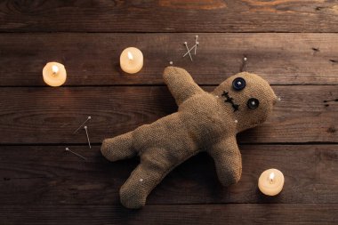 Tahta arka planda, dramatik ışıklandırması ve mumları olan bir vudu bebeği. Büyücülük ve kara sanat kavramı. Tahta arka planda bir çuval bezi bebek. Oyuncak bebeğe iğneler saplanmış. Boşluğu kopyala.