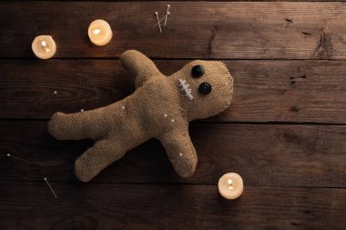 Tahta arka planda, dramatik ışıklandırması ve mumları olan bir vudu bebeği. Büyücülük ve kara sanat kavramı. Tahta arka planda bir çuval bezi bebek. Oyuncak bebeğe iğneler saplanmış. Boşluğu kopyala.