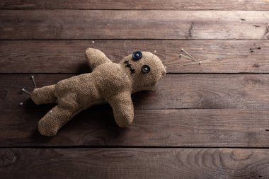 Voodoo doll on a wooden background with dramatic lighting. The concept of witchcraft and black art. Burlap doll on a wooden background. Pierce with maces. Copy space.