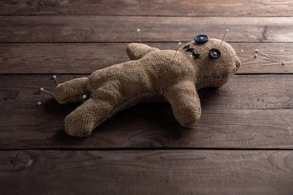 Voodoo doll on a wooden background with dramatic lighting. The concept of witchcraft and black art. Burlap doll on a wooden background. Pierce with maces. Copy space. — Stock Photo, Image