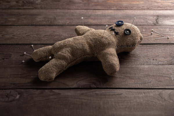 Voodoo doll on a wooden background with dramatic lighting. The concept of witchcraft and black art. Burlap doll on a wooden background. Pierce with maces. Copy space.