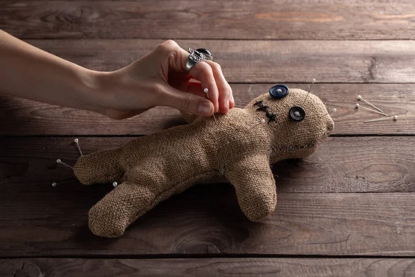 Boneca vodu em um fundo de madeira com iluminação dramática. O conceito de bruxaria e arte negra. Boneca de serapilheira em um fundo de madeira. Mãos espetam alfinetes numa boneca. Espaço de cópia . — Fotografia de Stock