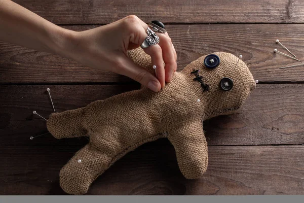 Voodoo doll on a wooden background with dramatic lighting. The concept of witchcraft and black art. Burlap doll on a wooden background. Hands stick pins into a doll. Copy space.