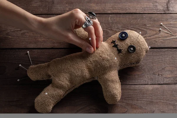 Muñeca vudú sobre fondo de madera con iluminación dramática. El concepto de brujería y arte negro. Muñeca de arpillera sobre fondo de madera. Las manos clavan alfileres en una muñeca. Copiar espacio . —  Fotos de Stock