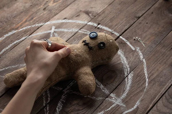 Muñeca vudú sobre fondo de madera con iluminación dramática. El concepto de brujería y arte negro y lo oculto. Muñeca de arpillera en el fondo de una estrella dibujada. Mano clavando alfileres en una muñeca . —  Fotos de Stock