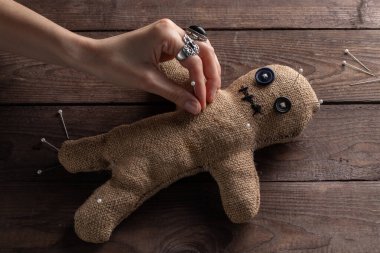 Voodoo doll on a wooden background with dramatic lighting. The concept of witchcraft and black art. Burlap doll on a wooden background. Hands stick pins into a doll. Copy space.