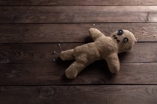 Voodoo doll on a wooden background with dramatic lighting. The concept of witchcraft and black art. Burlap doll on a wooden background. Pierce with maces. Copy space.