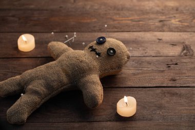 Tahta arka planda, dramatik ışıklandırması ve mumları olan bir vudu bebeği. Büyücülük ve kara sanat kavramı. Tahta arka planda bir çuval bezi bebek. Oyuncak bebeğe iğneler saplanmış. Boşluğu kopyala.