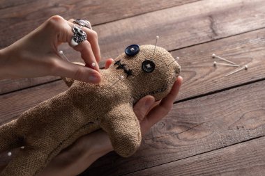 Voodoo doll on a wooden background with dramatic lighting. The concept of witchcraft and black art. Burlap doll on a wooden background. Hands stick pins into a doll. Copy space.