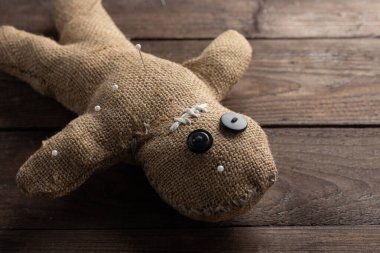 Voodoo doll on a wooden background with dramatic lighting. The concept of witchcraft and black art. Burlap doll on a wooden background. Pierce with maces. Copy space.