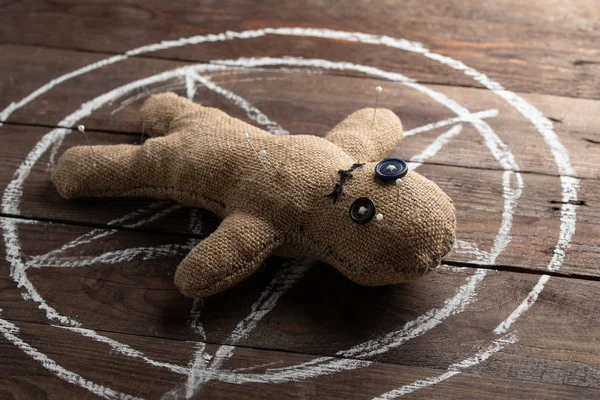 Muñeca vudú sobre fondo de madera con iluminación dramática. El concepto de brujería y arte negro y lo oculto. Muñeca de arpillera en el fondo de una estrella dibujada. Alfileres atascados en la muñeca . —  Fotos de Stock