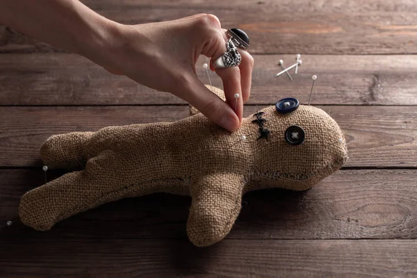 Voodoo doll on a wooden background with dramatic lighting. The concept of witchcraft and black art. Burlap doll on a wooden background. Hands stick pins into a doll. Copy space.