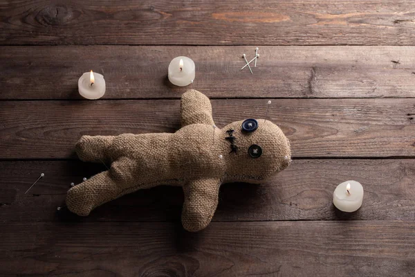 Voodoo pop op een houten achtergrond met dramatische verlichting en kaarsen. Het concept van hekserij en zwarte kunst. Jute pop op een houten achtergrond. Steek spelden in de pop. Kopieerruimte. — Stockfoto