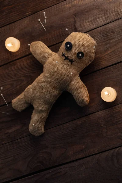 Voodoo doll on a wooden background with dramatic lighting and candles. The concept of witchcraft and black art. Burlap doll on a wooden background. Stuck pins in the doll. Copy space. — Stock Photo, Image