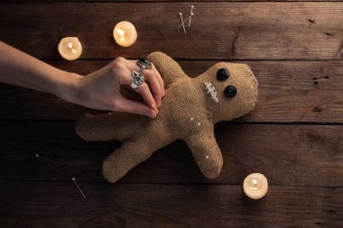 Tahta arka planda, dramatik ışıklandırması ve mumları olan bir vudu bebeği. Büyücülük ve kara sanat kavramı. Tahta arka planda bir çuval bezi bebek. Oyuncak bebeğe iğneler saplanmış. Boşluğu kopyala.
