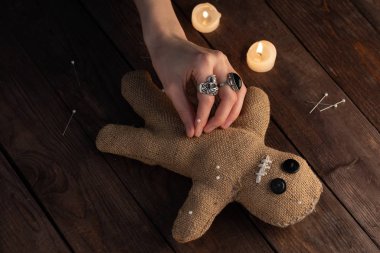 Voodoo doll on a wooden background with dramatic lighting and candles. The concept of witchcraft and black art. Burlap doll on a wooden background. Hands stick pins into a doll. Copy space.