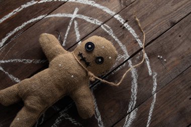 Tahta arka planda dramatik ışıklandırmalı bir vudu bebeği. Büyücülük, kara sanat ve okült kavramı. Çizilmiş bir yıldızın arka planındaki çuval bezi bebek. Oyuncak bebeğe iğneler saplanmış..