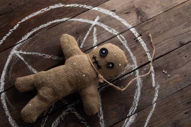 Tahta arka planda dramatik ışıklandırmalı bir vudu bebeği. Büyücülük, kara sanat ve okült kavramı. Çizilmiş bir yıldızın arka planındaki çuval bezi bebek. Oyuncak bebeğe iğneler saplanmış..