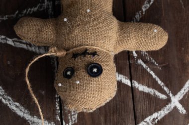 Tahta arka planda dramatik ışıklandırmalı bir vudu bebeği. Büyücülük, kara sanat ve okült kavramı. Çizilmiş bir yıldızın arka planındaki çuval bezi bebek. Oyuncak bebeğe iğneler saplanmış..