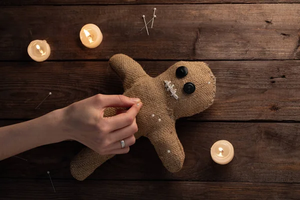 Muñeca vudú sobre fondo de madera con iluminación dramática y velas. El concepto de brujería y arte negro. Muñeca de arpillera sobre fondo de madera. Las manos clavan alfileres en una muñeca. Copiar espacio . —  Fotos de Stock