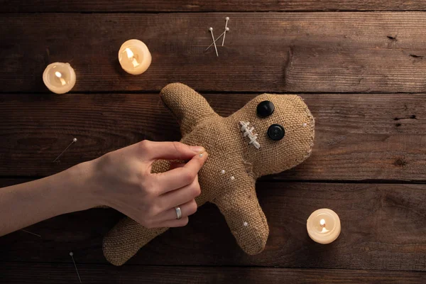 Muñeca vudú sobre fondo de madera con iluminación dramática y velas. El concepto de brujería y arte negro. Muñeca de arpillera sobre fondo de madera. Las manos clavan alfileres en una muñeca. Copiar espacio . —  Fotos de Stock