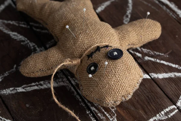 Voodoo doll on a wooden background with dramatic lighting. The concept of witchcraft and black art and the occult. Burlap doll on the background of a drawn star. Stuck pins in the doll. — Stock Photo, Image