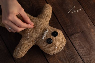 Voodoo doll on a wooden background with dramatic lighting. The concept of witchcraft and black art. Burlap doll on a wooden background. Hands stick pins into a doll. Copy space.