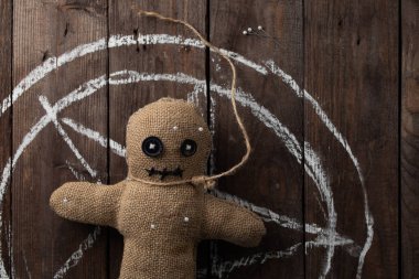 Tahta arka planda dramatik ışıklandırmalı bir vudu bebeği. Büyücülük, kara sanat ve okült kavramı. Çizilmiş bir yıldızın arka planındaki çuval bezi bebek. Oyuncak bebeğe iğneler saplanmış..